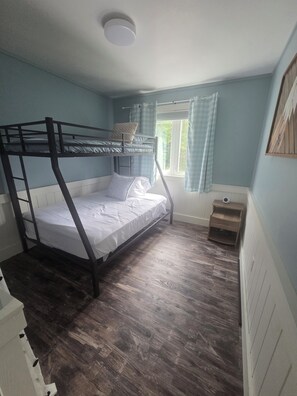 A bunk bed room with a window, a bedside table, and a small cabinet.