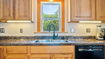 A kitchen with wooden cabinets, a stainless steel sink, a Bosch dishwasher, and a window with a view of greenery.