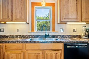 A kitchen with wooden cabinets, a stainless steel sink, a Bosch dishwasher, and a window with a view of greenery.