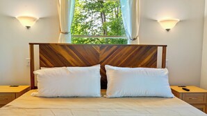 Ein ordentlich bezogenes Bett mit zwei Kissen, einem Holz-Kopfteil, Nachttischen und einem Fenster mit Vorhängen.