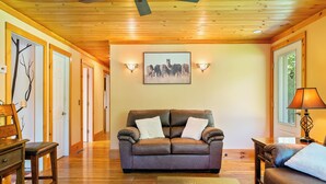 Ein Wohnzimmer mit einem braunen Ledersofa, einem Holztisch und einer Lampe. An der Wand hängt ein gerahmtes Bild und eine Deckenleuchte ist angebracht.