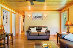 A living room with a brown leather sofa, a wooden coffee table, and a lamp. There is a framed picture on the wall and a ceiling fan.