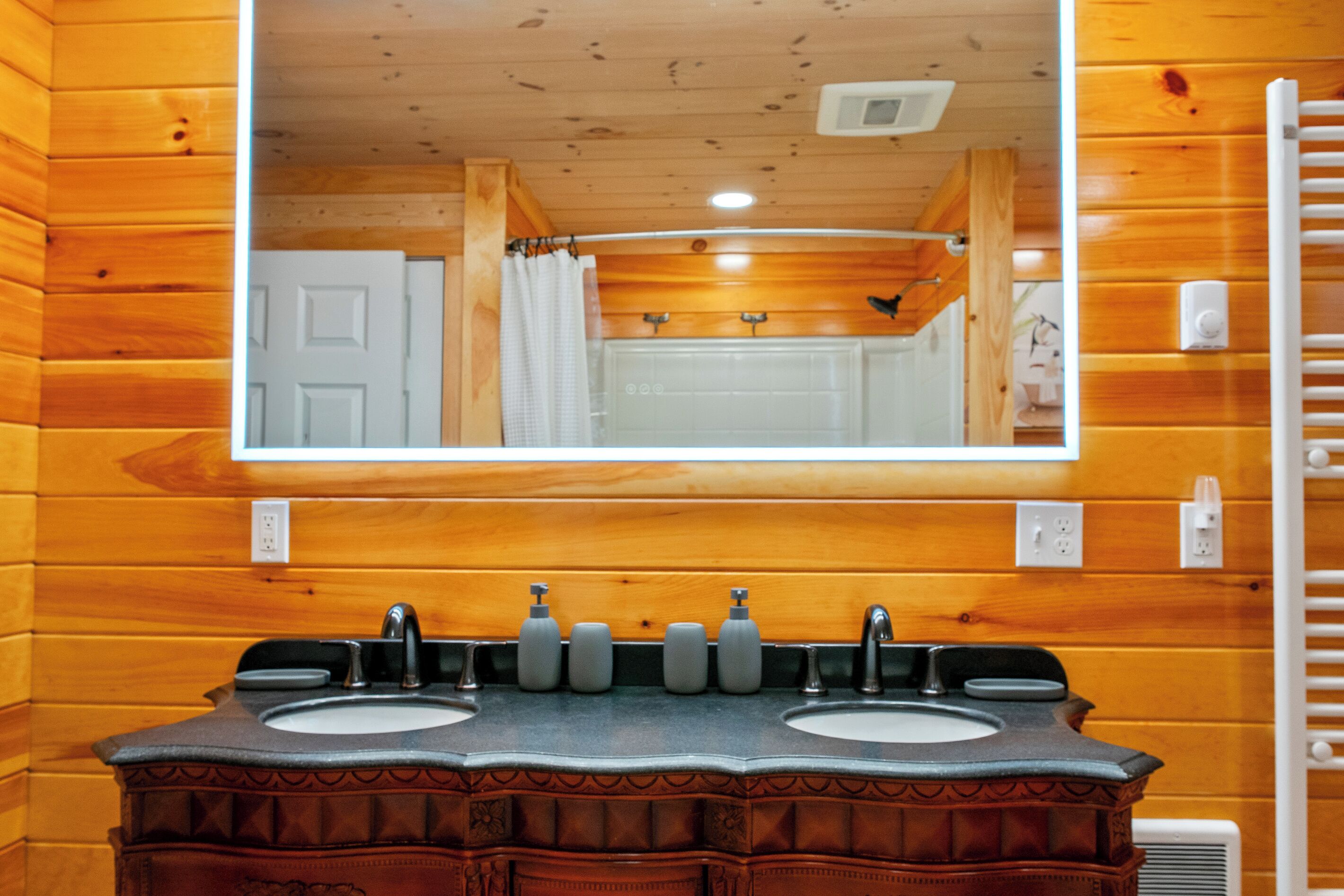 A bathroom with wooden walls, a double sink vanity, and a mirror above the sinks.