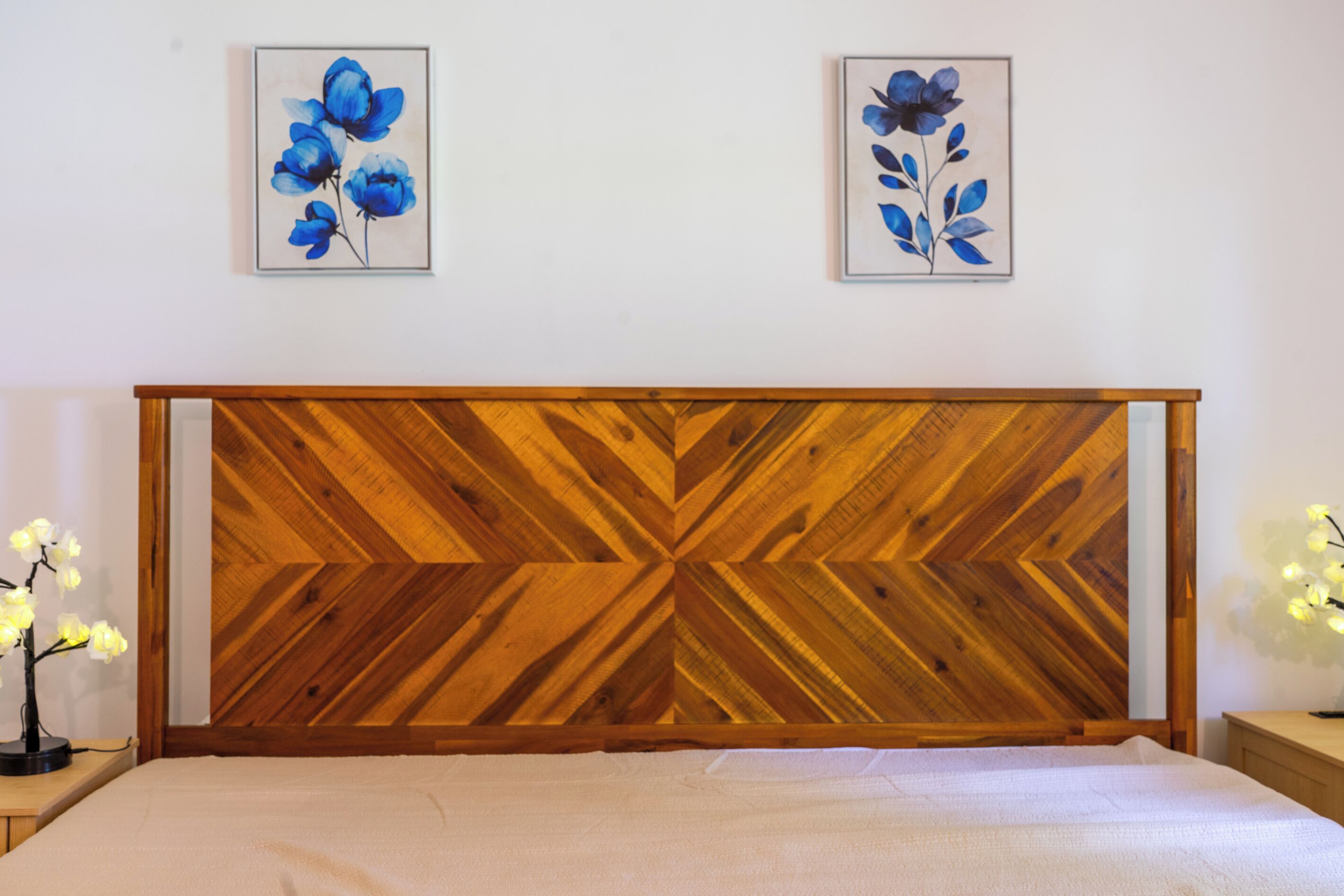 A bedroom with a wooden headboard, a bed, bedside tables, and two framed floral paintings on the wall.