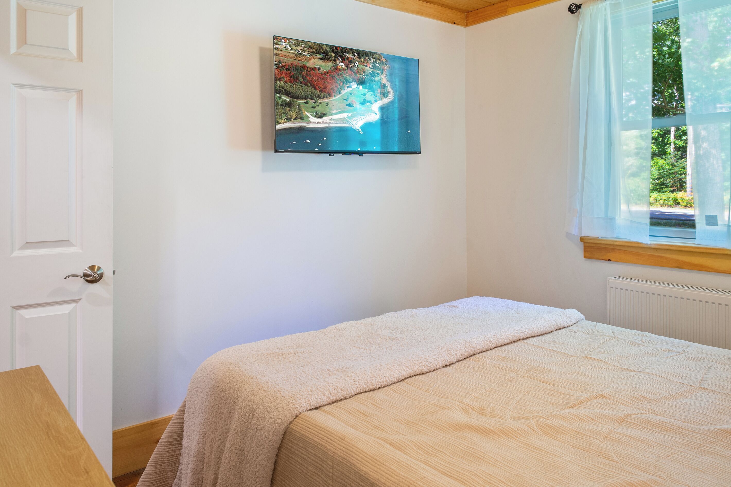Ein Schlafzimmer mit einem Bett, einem Bild an der Wand und einem Fenster mit Vorhängen.