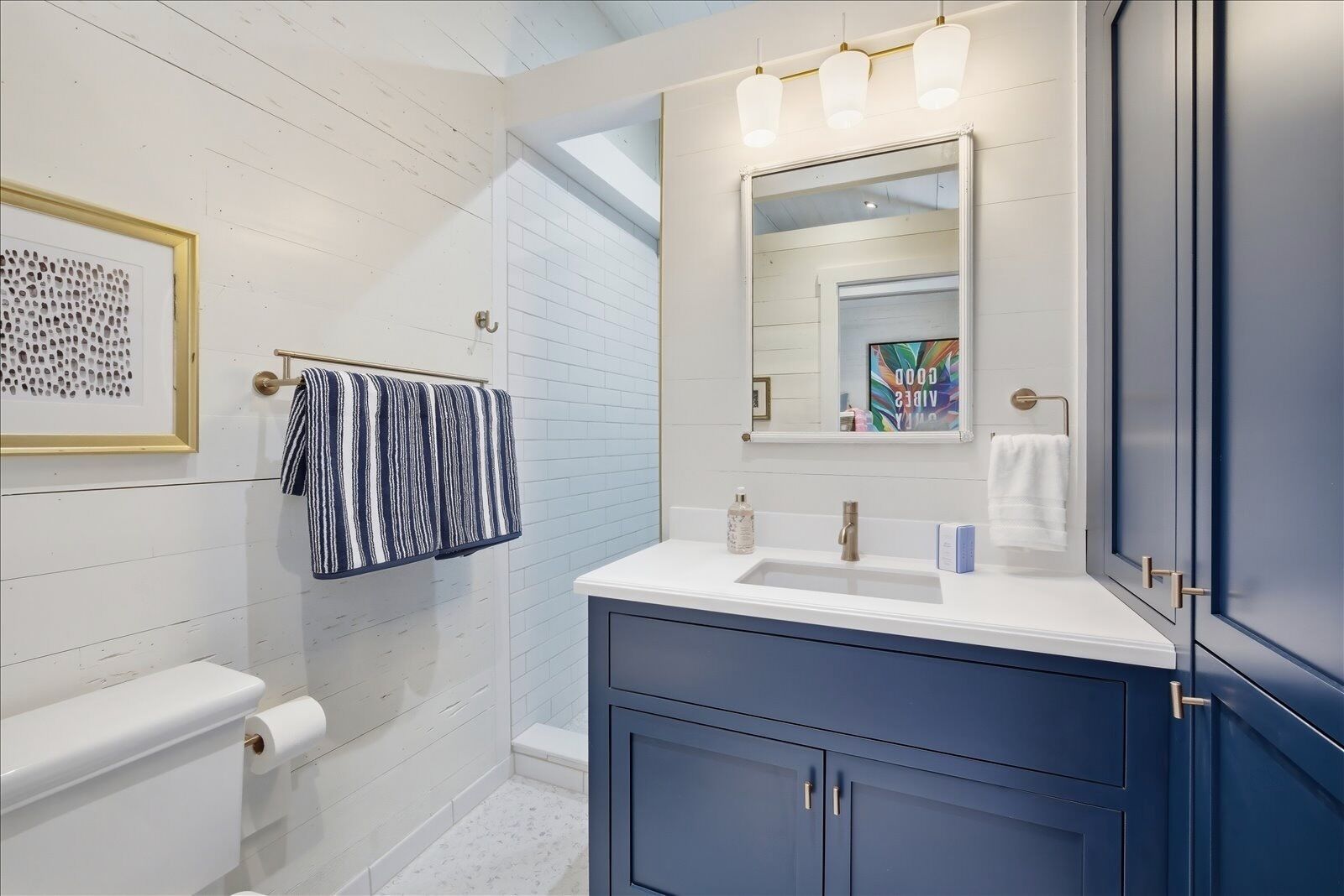 Ein Badezimmer mit einer weißen Toilette, einem blauen Waschtisch mit Spiegel und einem Handtuchhalter mit gestreiftem Handtuch.