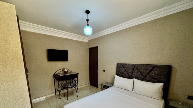 A hotel room with a bed, a desk, a chair, a flat-screen TV, and a ceiling light. - HOTEL BEACH CLUB LA PERLE (Casablanca)