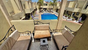 A balcony with two cushioned chairs and a small table, overlooking a swimming pool and a building with a sign that reads 'Hotel'. - HOTEL BEACH CLUB LA PERLE (Casablanca)