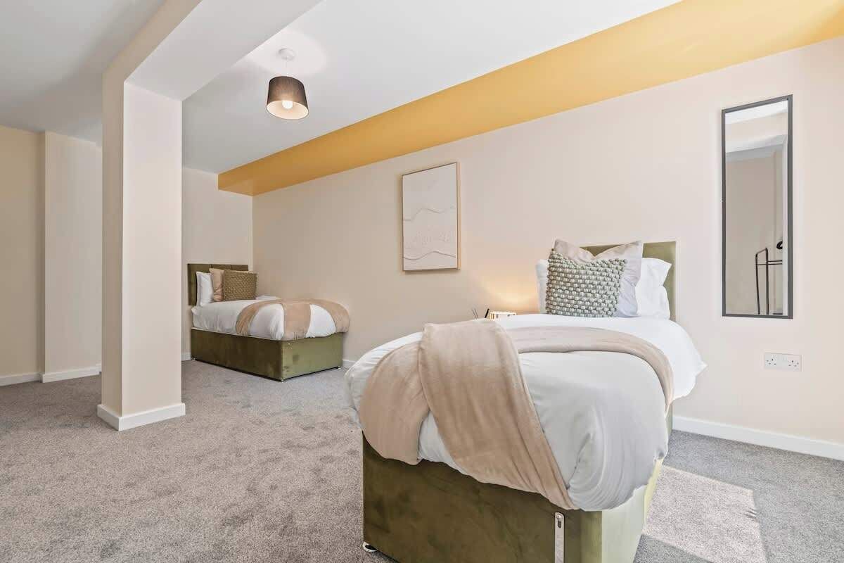 A bedroom with a large bed, a smaller bed in the background, a bedside table, a wall-mounted mirror, and a ceiling light fixture.
