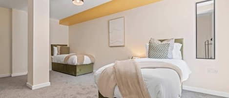 A bedroom with a large bed, a smaller bed in the background, a bedside table, a wall-mounted mirror, and a ceiling light fixture.