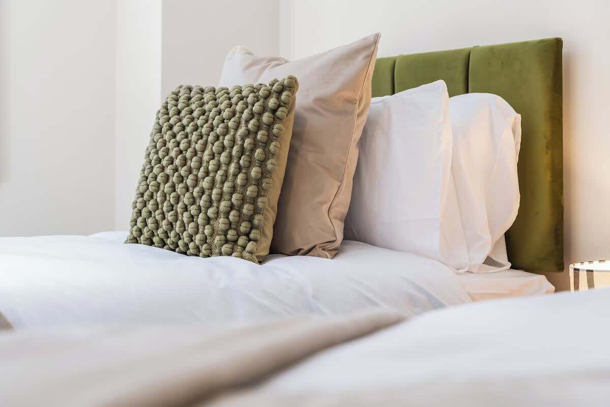A bed with a green upholstered headboard, white bedding, and a textured green pillow.