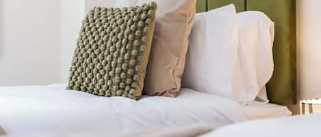 A bed with a green upholstered headboard, white bedding, and a textured green pillow.