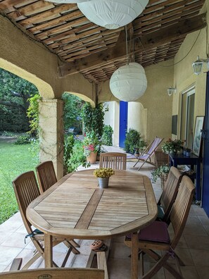 Eine Terrasse im Freien mit einem Holztisch und Stühlen, umgeben von Kübelpflanzen und Blick auf den Garten.