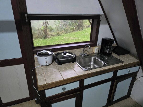 A small kitchenette with a window, a coffee maker, a slow cooker, and a sink.
