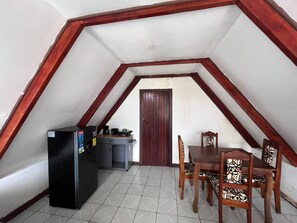 A small kitchenette with a refrigerator and a coffee machine, a dining table with chairs, and a door leading to another room. - Tranquil Cabin Getaway in San Ramón, Costa Rica (La Unión)
