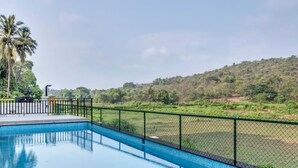 A swimming pool with a view of a green landscape and a hill in the distance. - 2bhk With Pool nr Candolim Beach Palms By Umiya (Candolim)