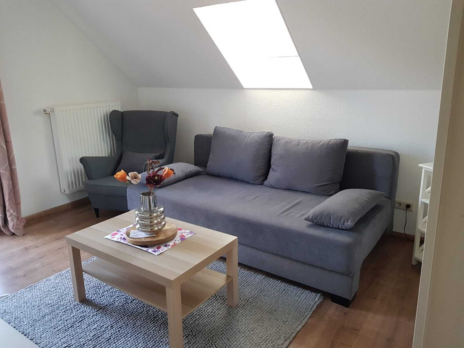 Ein modernes Wohnzimmer mit einem grauen Sofa, einem kleinen Holztisch mit einer Vase und einem Oberlicht.