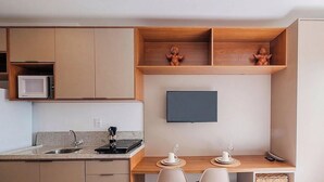 Uma cozinha compacta com eletrodomésticos embutidos, uma televisão de tela plana e um espaço de jantar com mesa e cadeiras.