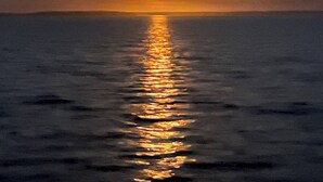 Ein Sonnenuntergang über einem ruhigen Meer mit der sichtbaren Spiegelung der Sonne an der Wasseroberfläche.