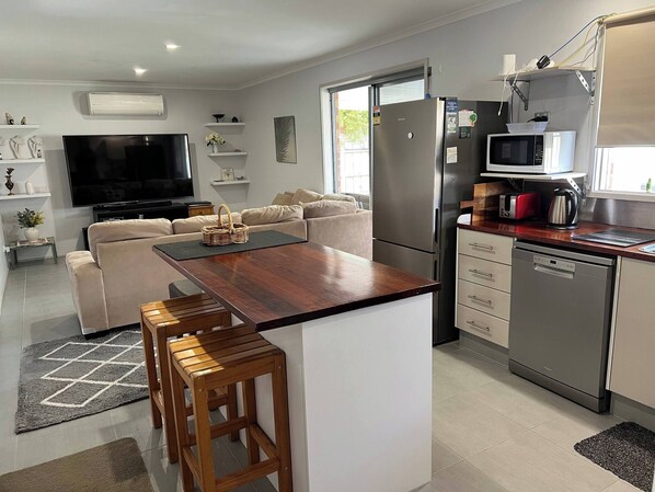 A modern kitchen with a central island, a dining area with wooden stools, a sofa, and a flat-screen TV.