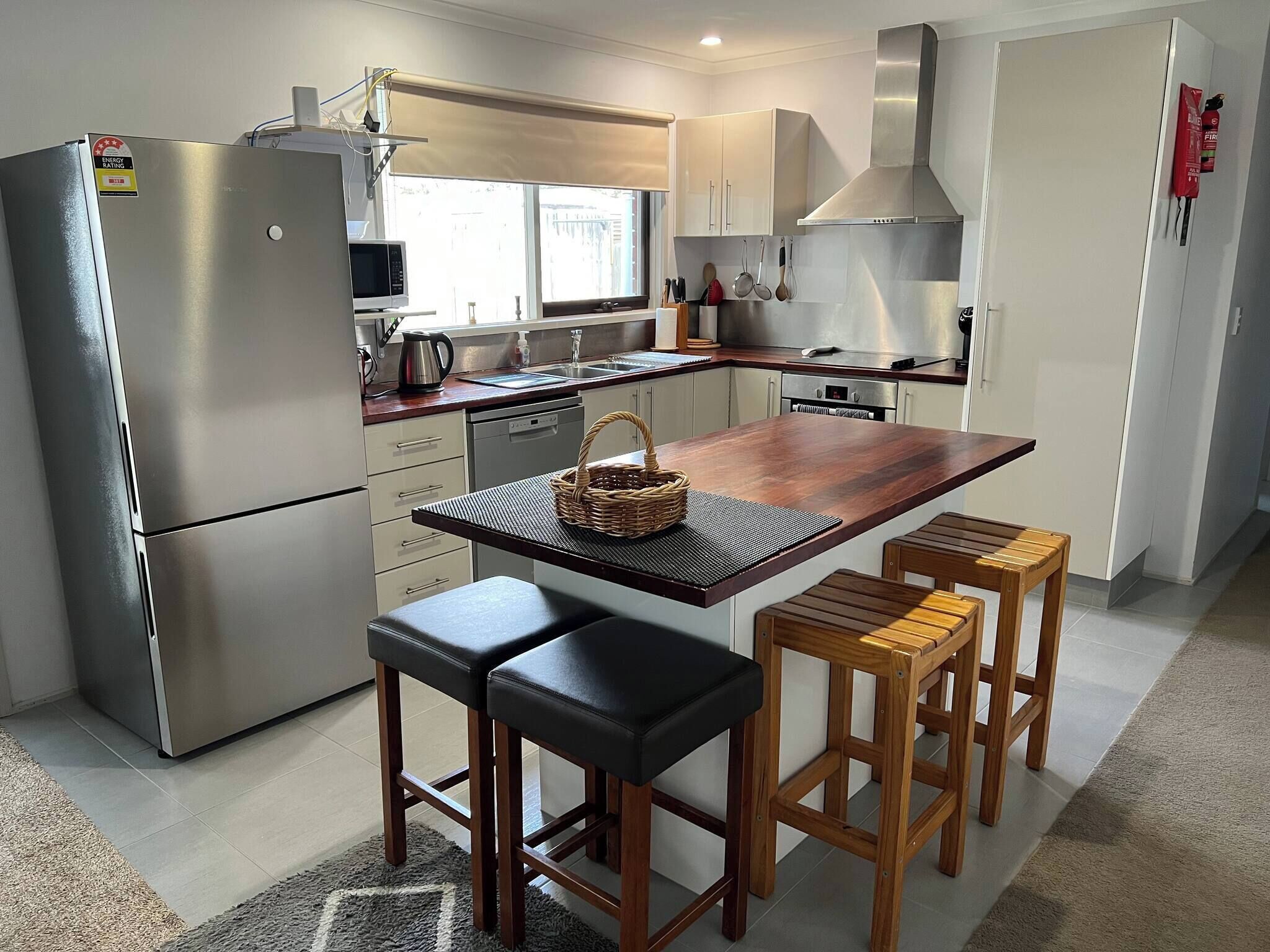 A modern kitchen with a stainless steel refrigerator, a wooden island with stools, and a large stove.