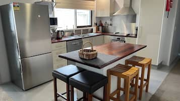 A modern kitchen with a stainless steel refrigerator, a wooden island with stools, and a large stove.