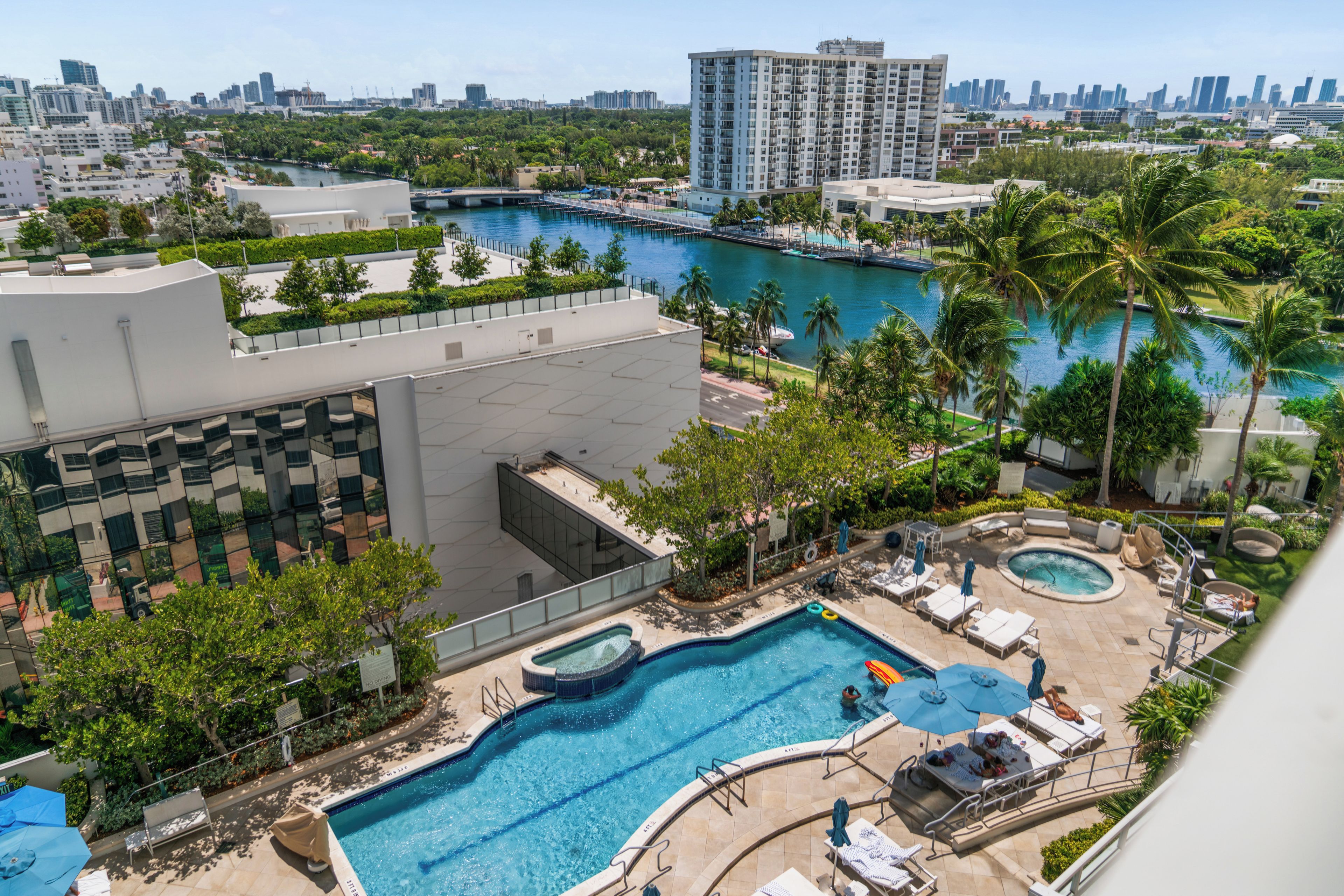 A rooftop pool area with multiple swimming pools, lounge chairs, and palm trees.