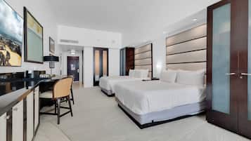 A hotel room with two beds, a desk, and a chair. There is a large painting on the wall and a wardrobe with a mirror.