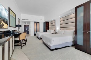 A hotel room with two beds, a desk, and a chair. There is a large painting on the wall and a wardrobe with a mirror. - Fontainebleau Miami Resort (Miami Beach)