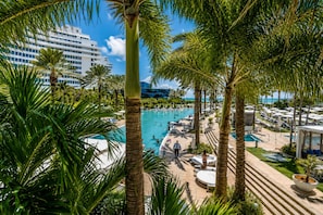 A resort pool area with palm trees, lounge chairs, and a large building in the background. - Fontainebleau Miami Resort (Miami Beach)