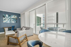A modern living room with a grey sofa, a wooden chair, a round table, and a large window with a view of a building. - Fontainebleau Miami Resort (Miami Beach)