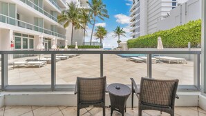A balcony with wicker chairs and a view of a pool area with lounge chairs and palm trees. - Fontainebleau Miami Resort (Miami Beach)