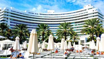 Um hotel com fachada curva, várias varandas e área de piscina com espreguiçadeiras e guarda-sóis.