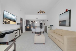 A modern living room with a sofa, a dining area with chairs, a kitchen in the background, and a large TV on the wall. - Fontainebleau Miami Resort (Miami Beach)
