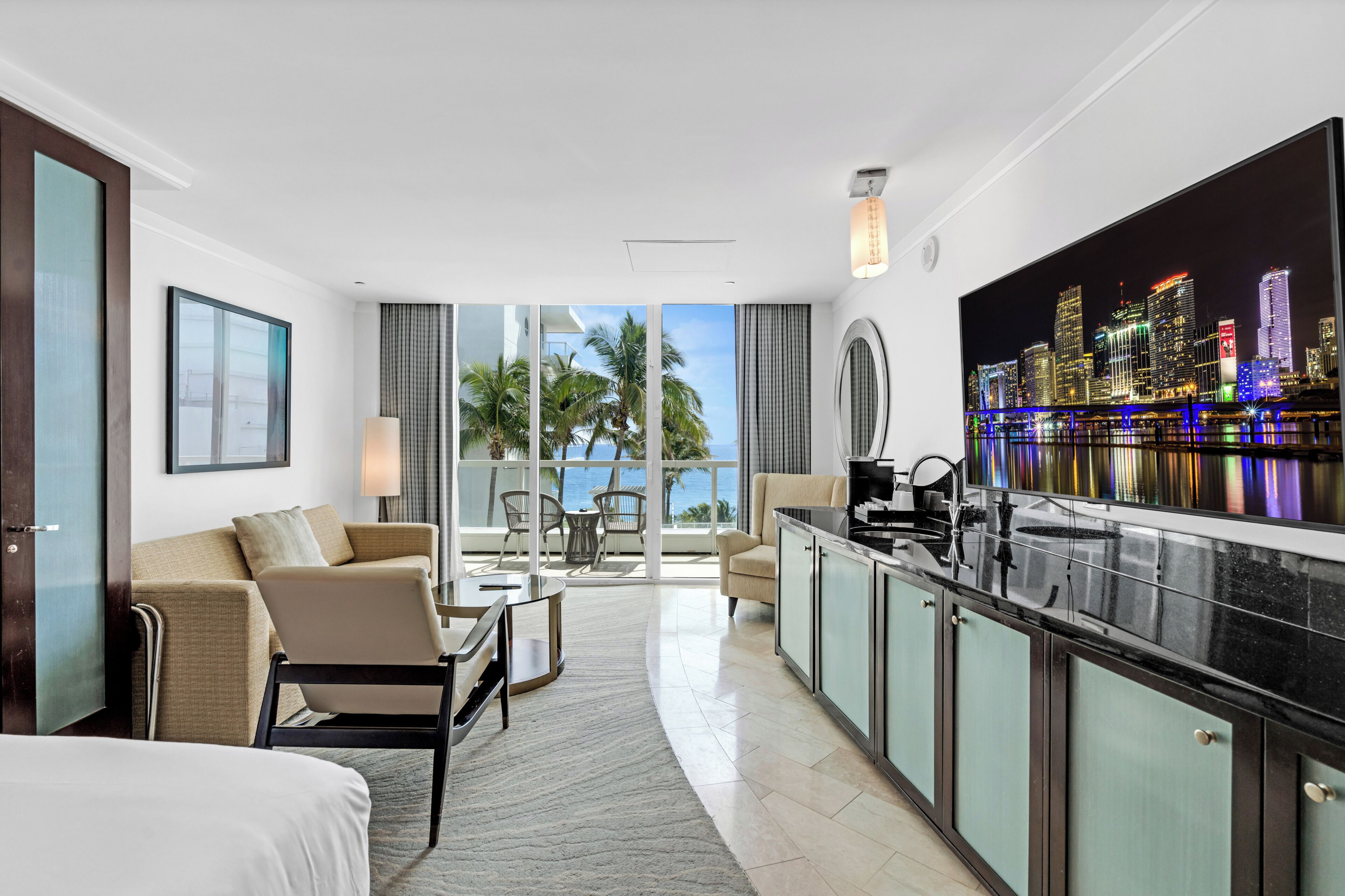 Quarto de hotel moderno com varanda, área de refeições e ampla vista panorâmica da cidade.