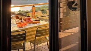Un balcón con una mesa lista para comer, con vista a un paisaje pintoresco con montañas y una masa de agua.