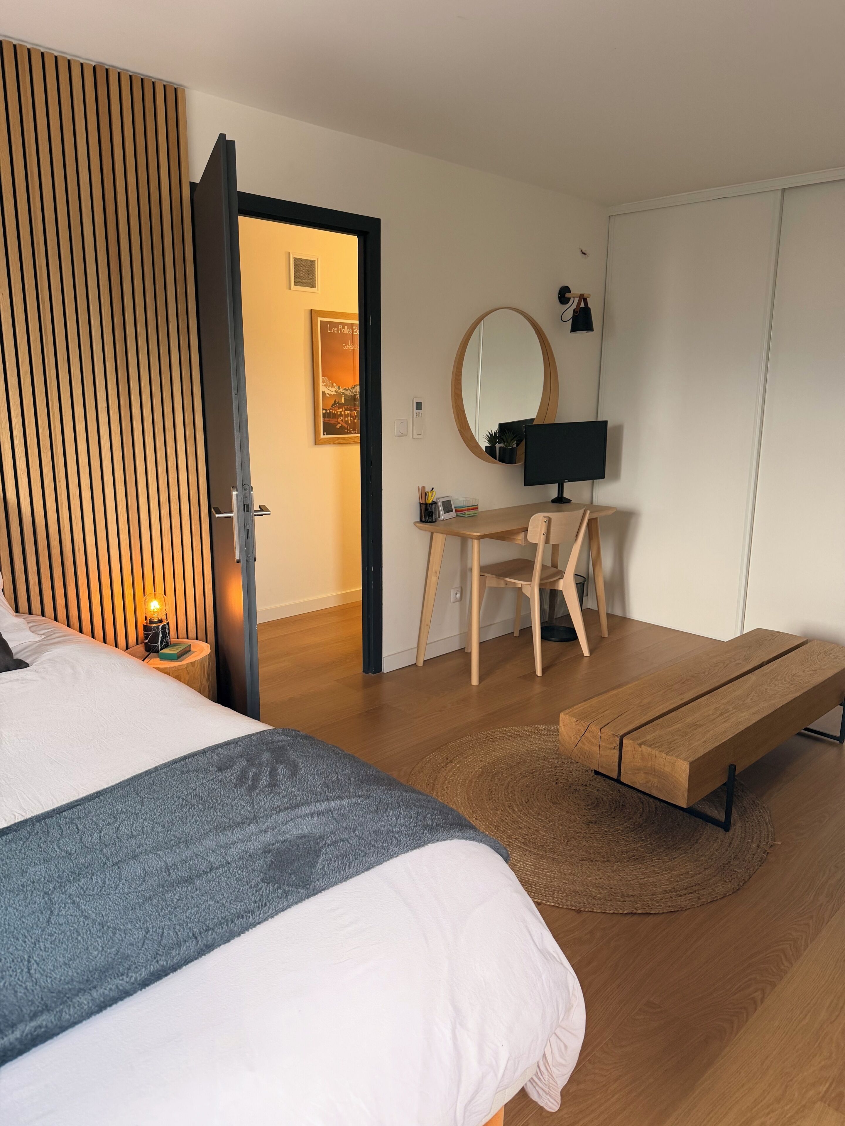 A bedroom with a bed, bedside table, desk, chair, and a bench.