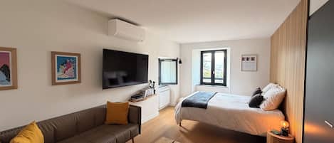 A modern bedroom with a bed, a sofa, a TV, and a window.