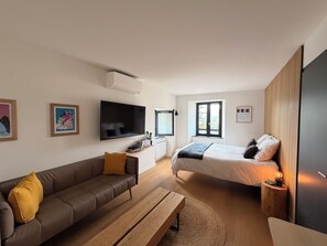 A modern bedroom with a bed, a sofa, a TV, and a window.