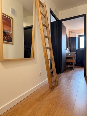 A wooden ladder leaning against a wall in a hallway with a door leading to a room with a dark-colored cabinet and a window.