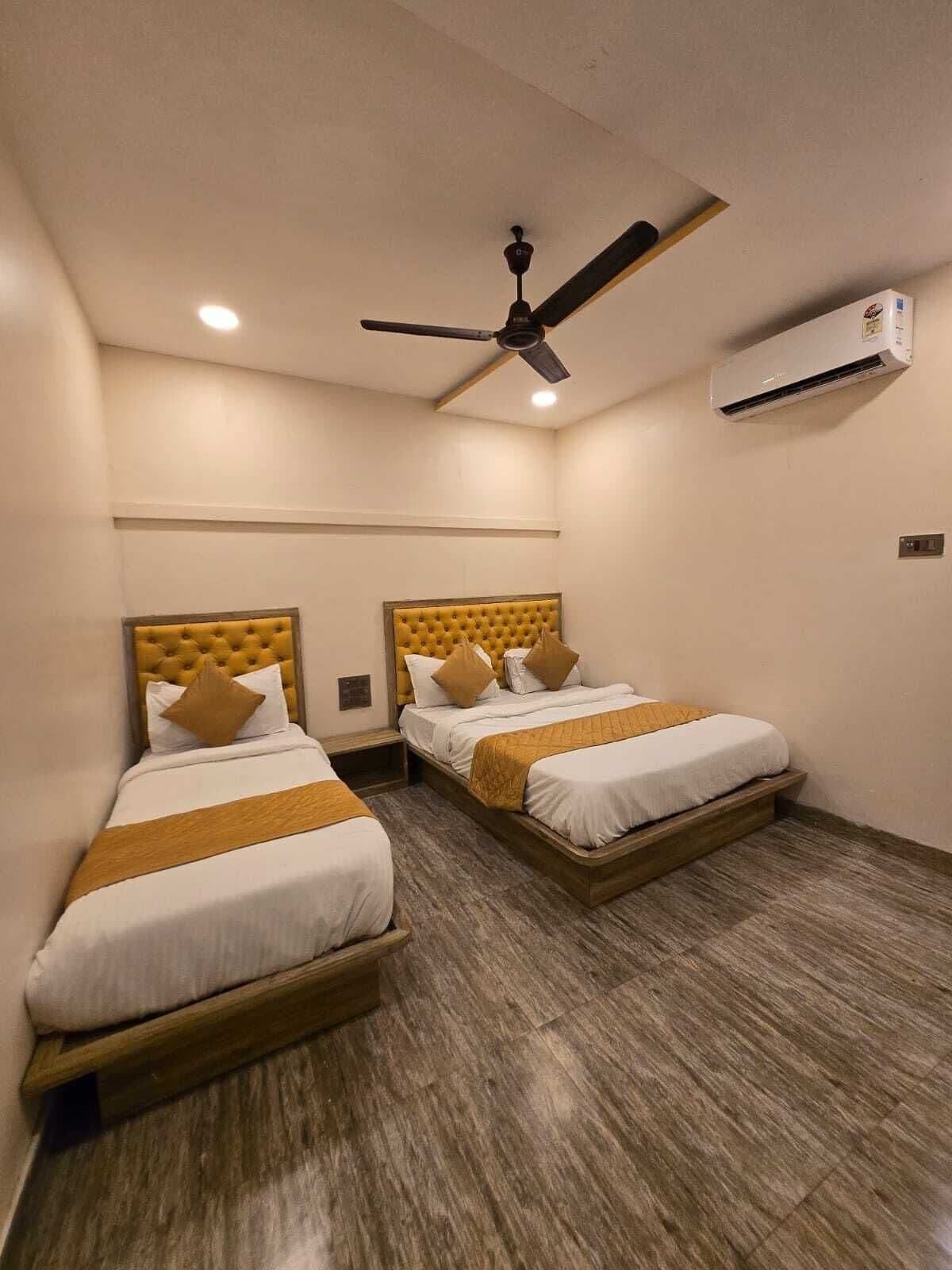 Ein Hotelzimmer mit zwei Betten, einem Deckenventilator, einer Klimaanlage und Holzboden.