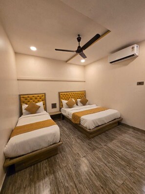 A hotel room with two beds, a ceiling fan, an air conditioning unit, and a wooden floor. - Hotel Royce BKC (Mumbai)