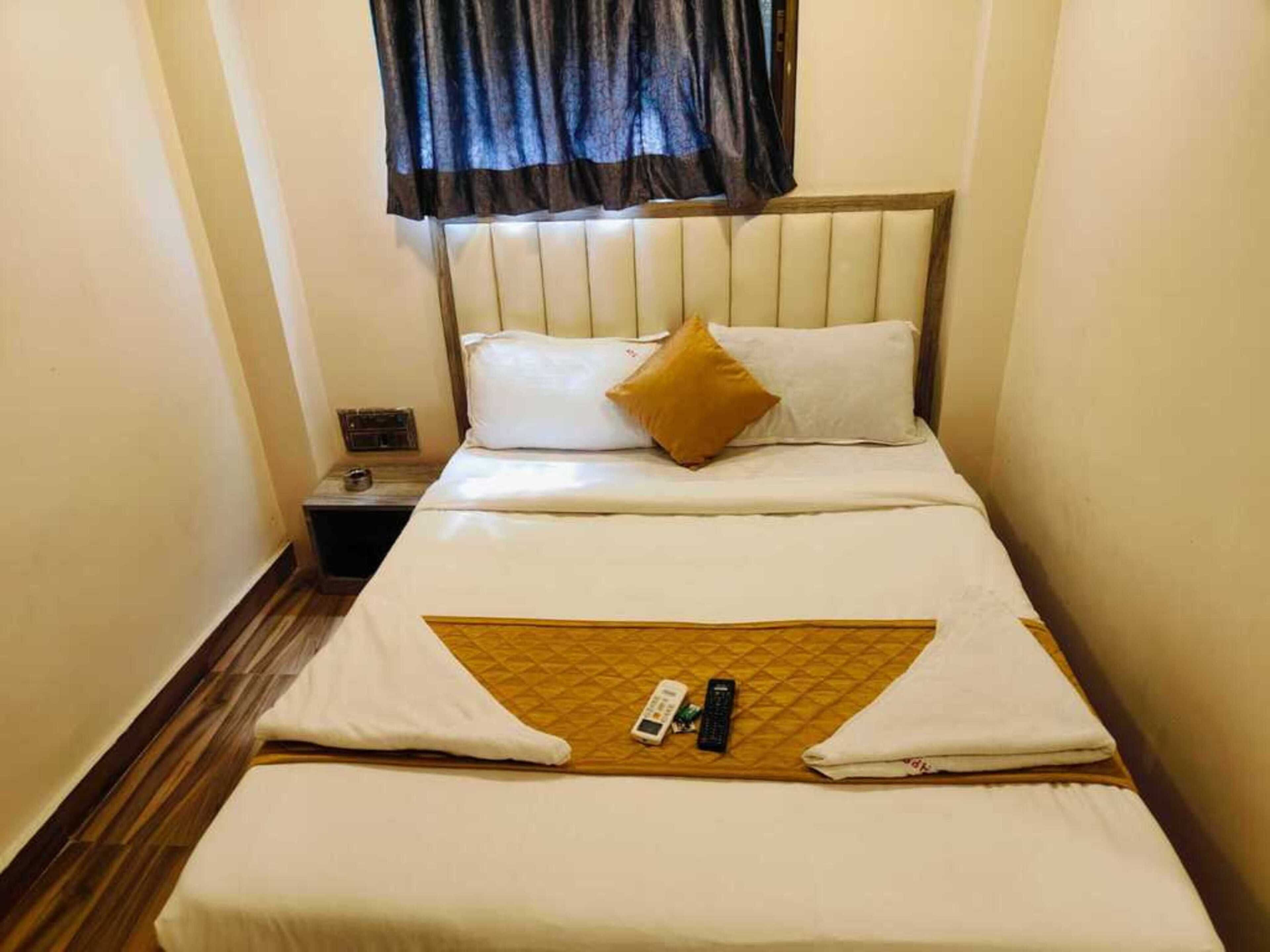Une chambre d’hôtel avec un lit, des oreillers, une table de chevet et une fenêtre avec des rideaux.