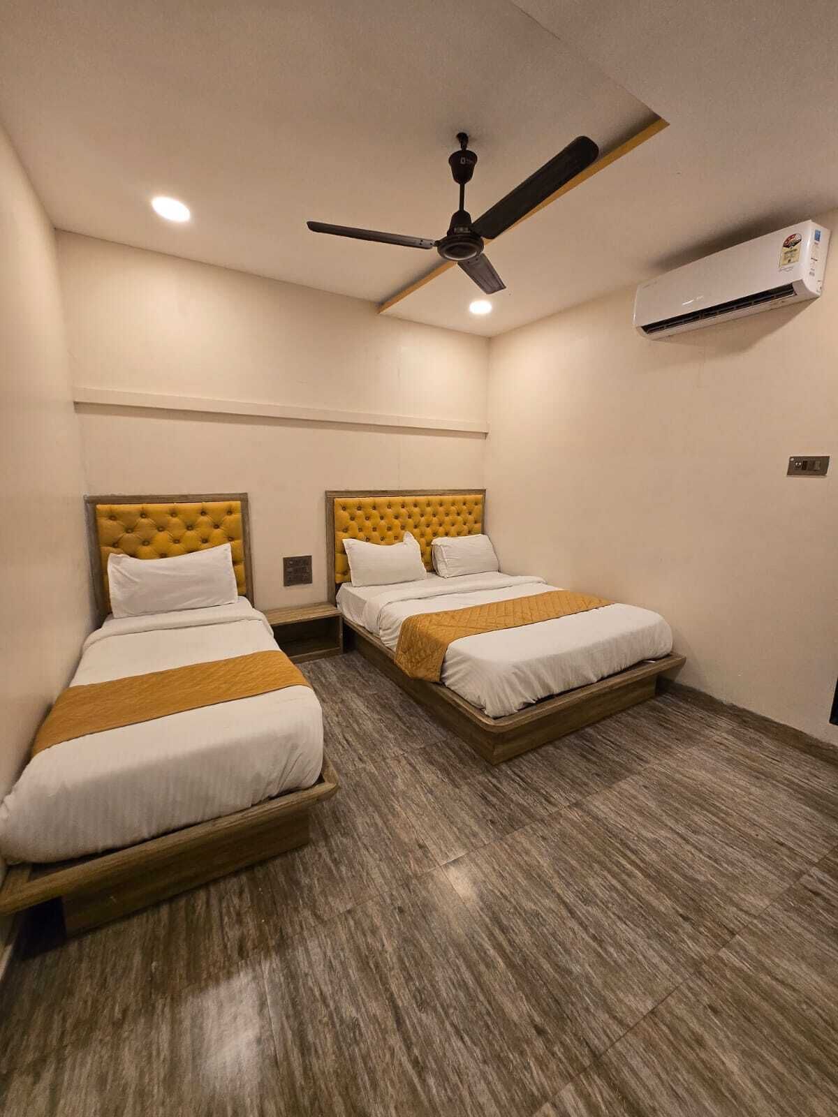 A hotel room with two single beds, a ceiling fan, an air conditioning unit, and a wooden floor.