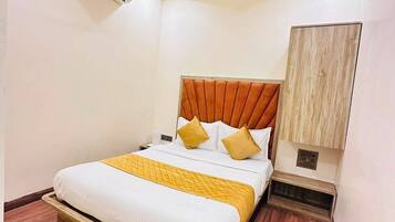 A hotel room with a bed, a ceiling fan, an air conditioning unit, and a wooden floor.