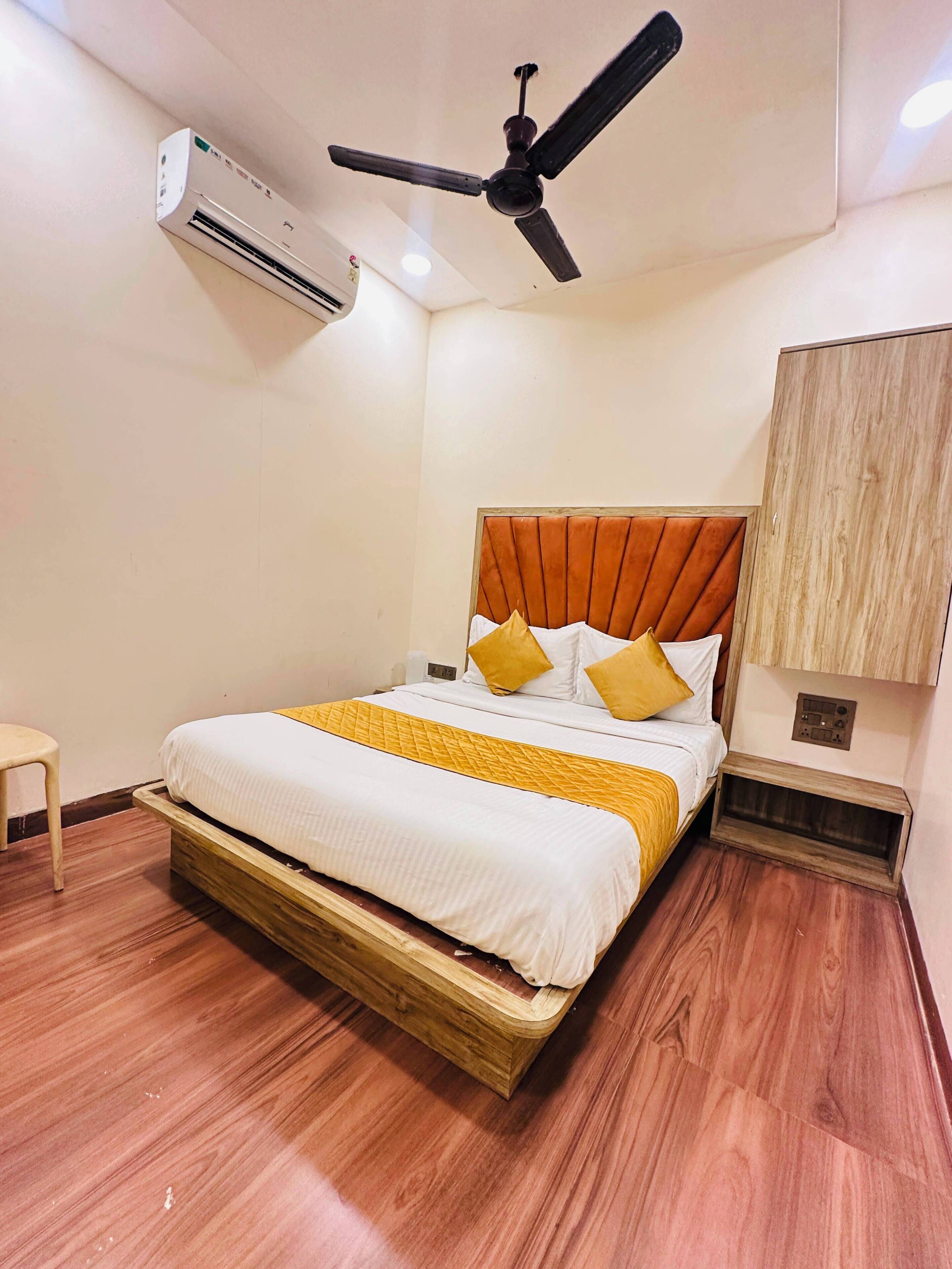 A bedroom with a bed, a ceiling fan, an air conditioning unit, and a wooden floor.
