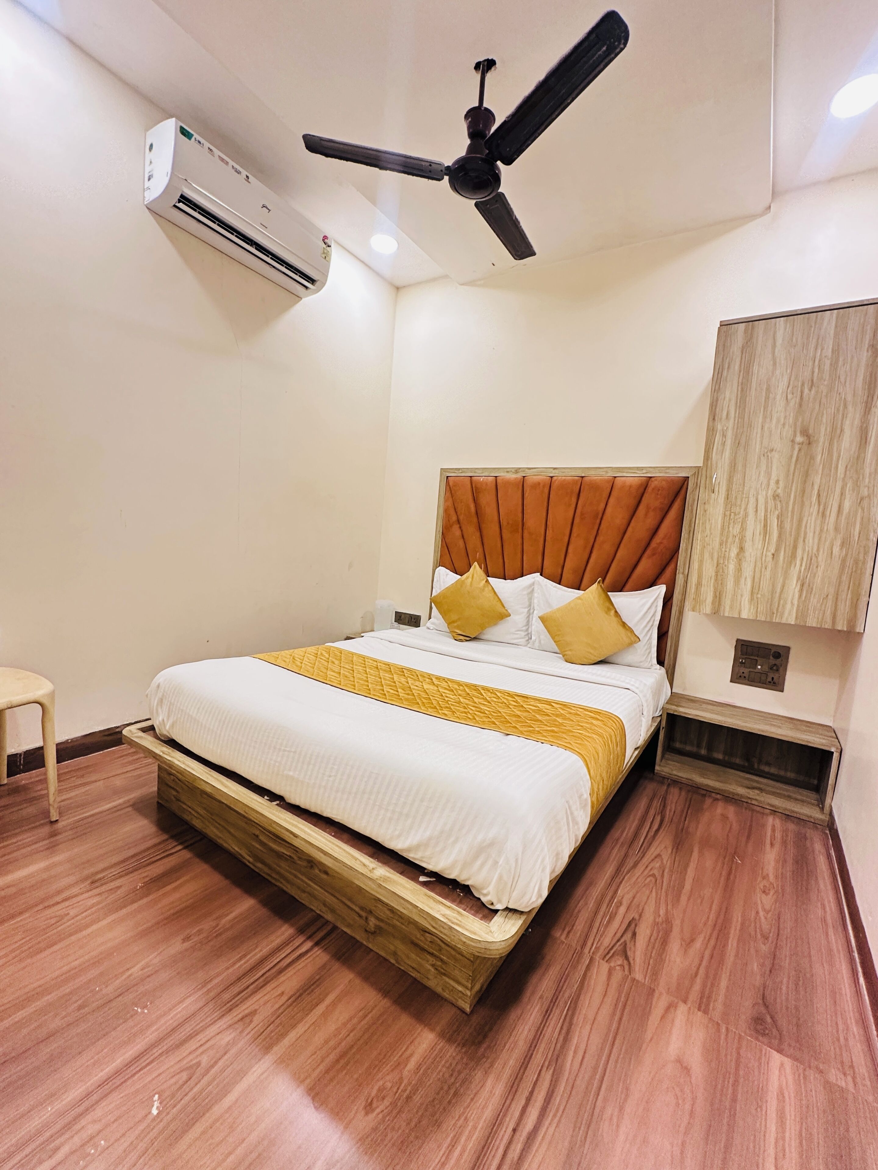 A bedroom with a bed, a ceiling fan, an air conditioning unit, a wooden floor, and a wardrobe.