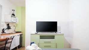 Een kleine kamer met een bed, een bureau met een computermonitor, een magnetron en een stoel.