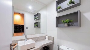 Ein modernes Badezimmer mit einem weißen Waschbecken, einem Spiegel und grauen Regalen mit Pflanzen.