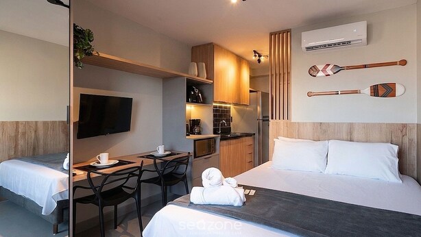 Ein Hotelzimmer mit Bett, Schreibtisch, Stuhl, Fernseher, Minibar und Wandklimaanlage.